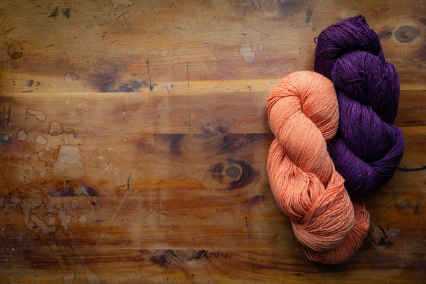 Deux écheveaux torsadés de fil en violet et orange sur un vieux dessus de table en bois, thème tricot et crochet, espace de copie créatif, aspect horizontal
 - Photo, image