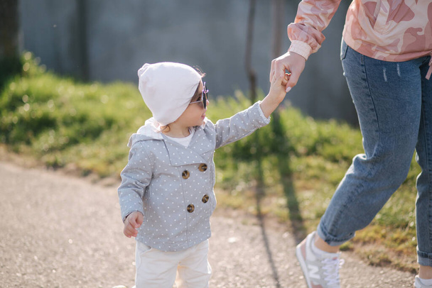 Szczęśliwa dziewczynka spaceruje z matką w parku. Mama i córka spacerują niedaleko promenady w Dzień Matki. Cute little girl w okularach przeciwsłonecznych - Zdjęcie, obraz