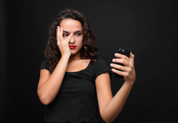 young pretty woman feeling bored, frustrated and sleepy after a tiresome, dull and tedious task, holding face with hand holding a smartphone - Photo, Image