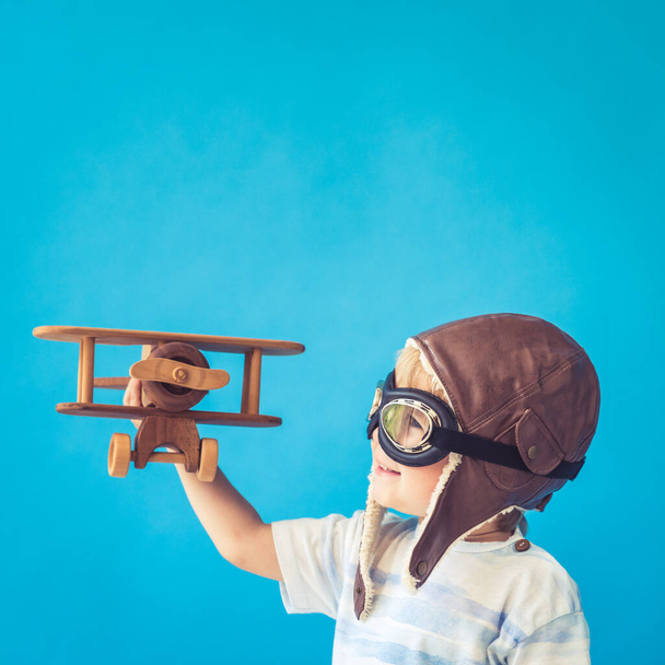 Happy child playing with vintage wooden airplane. Kid having fun against blue background. Imagination and freedom concept - Fotografie, Obrázek