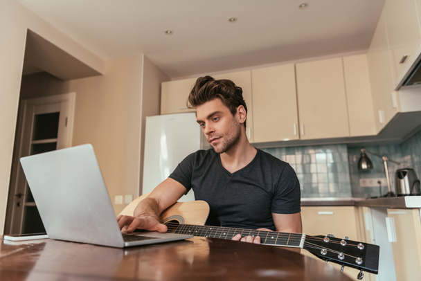 handsome young man with guitar using laptop in kitchen - Photo, Image