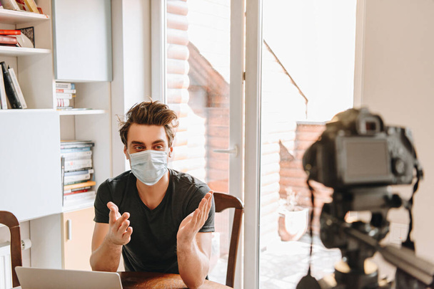foyer sélectif du jeune blogueur vidéo dans la gestuelle masque médical tout en regardant appareil photo numérique
 - Photo, image