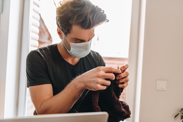 jeune homme en masque médical tricot près d'un ordinateur portable à la maison
 - Photo, image