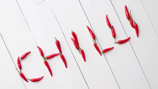 Μια λέξη που σχηματίστηκε με μικρές κόκκινες πιπεριές τσίλι. Τοποθετείται σε λευκό ξύλινο τραπέζι - Πλάνα, βίντεο