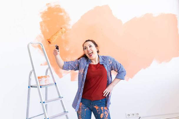 Dancing funny woman painting the walls of new home. Renovation, repair and redecoration concept. - Photo, Image