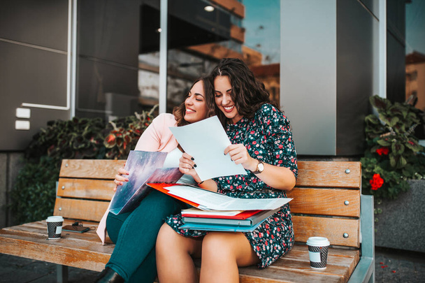 Happy female friends, students reading document together, good news, while sitting outdoors. Two cheerful women celebrating success. - Photo, Image