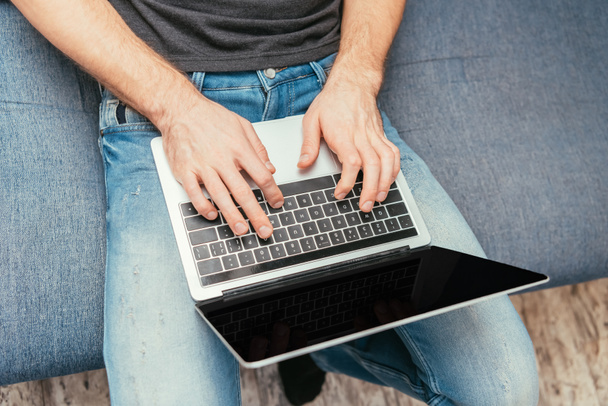 vista ritagliata dell'uomo in jeans denim digitando sul computer portatile con schermo vuoto, vista dall'alto
 - Foto, immagini