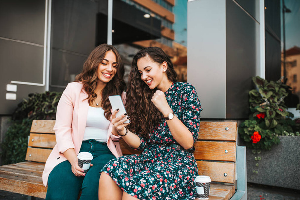 Dos amigas felices celebrando el éxito mientras leen buenas noticias en un smartphone al aire libre en la calle de la ciudad
. - Foto, imagen
