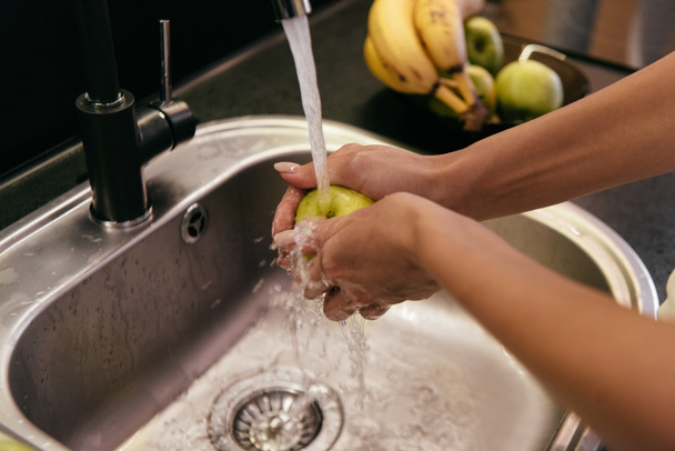 cropped view of girl washing fruits in washbasin during quarantine - Foto, afbeelding