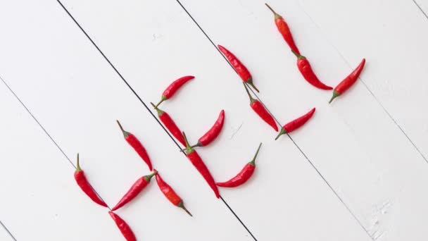 Μια λέξη που σχηματίζεται με μικρές κόκκινες πιπεριές τσίλι. Τοποθετείται σε λευκό ξύλινο τραπέζι - Πλάνα, βίντεο