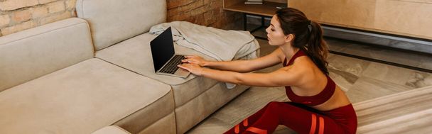 hermosa deportista de entrenamiento en línea con el ordenador portátil en la alfombra de fitness en casa durante el autoaislamiento, orientación panorámica
 - Foto, imagen