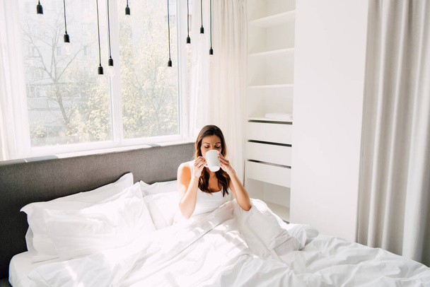 aantrekkelijke vrouw drinken koffie in bed in de ochtend tijdens zelfisolatie - Foto, afbeelding