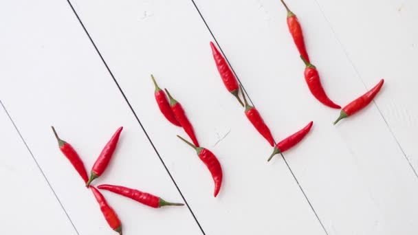 Słowo KILL utworzone z małych czerwonych papryczek chili. Umieszczony na białym drewnianym stole - Materiał filmowy, wideo