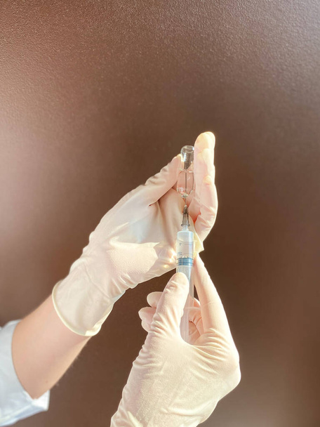 A fair-skinned woman doctor / medical worker in a white coat and disposable gloves holds an open ampoule with a medicine and a syringe in her hands.Free space. - Photo, Image