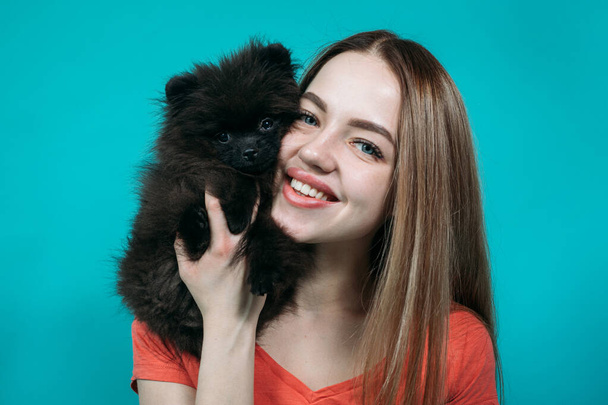 νεαρή κοπέλα με μακριά μαλλιά και μαύρο σπιτζ της χαμογελώντας και γελώντας σε ένα μπλε φόντο στο στούντιο - Φωτογραφία, εικόνα