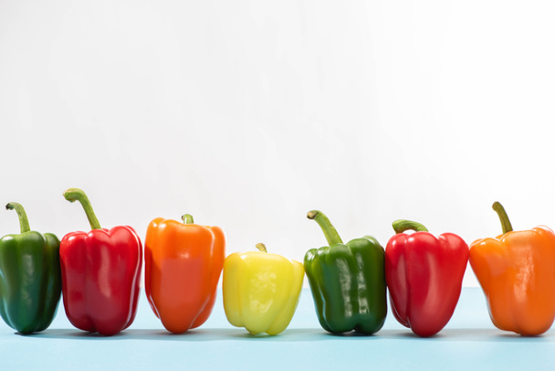 fresh colorful bell peppers on blue surface on white background - Foto, afbeelding