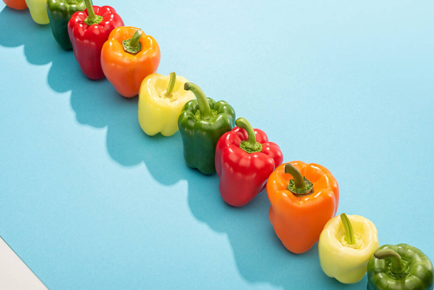 fresh colorful bell peppers in row on blue surface - Foto, Imagen
