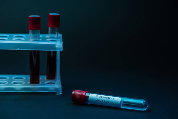 Vacina contra o Coronavirus perto da cremalheira do tubo de ensaio com amostras de sangue no escuro
 - Foto, Imagem