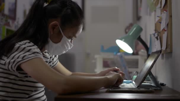 Grundschülerin mit Mundschutz und digitalem Tablet für den Online-Unterricht zu Hause. Teenager schreiben während des Studiums von zu Hause aus an einem Buch mit Videoanruf während der COVID-19-Pandemiesituation. - Filmmaterial, Video