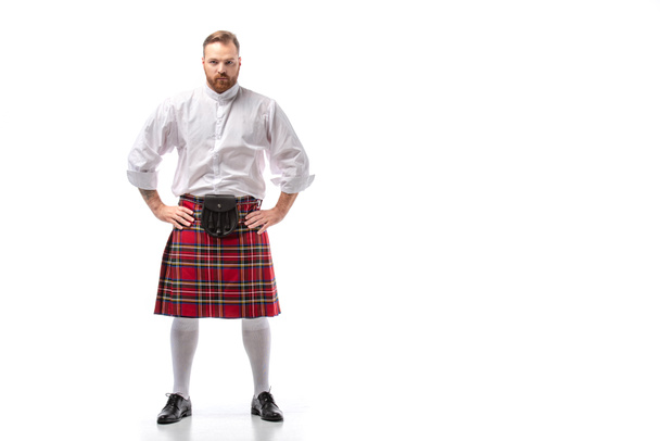 serious Scottish redhead man in red kilt with hands on hips on white background - Photo, Image
