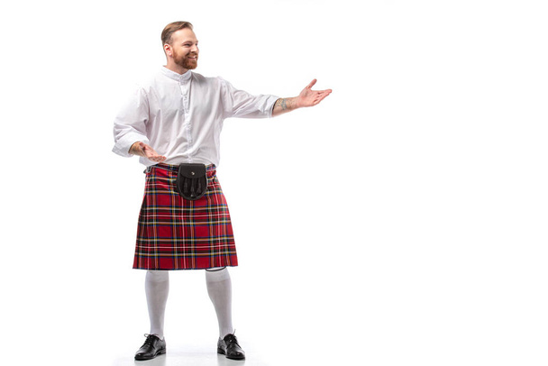 smiling Scottish redhead man in red kilt gesturing on white background - Fotó, kép