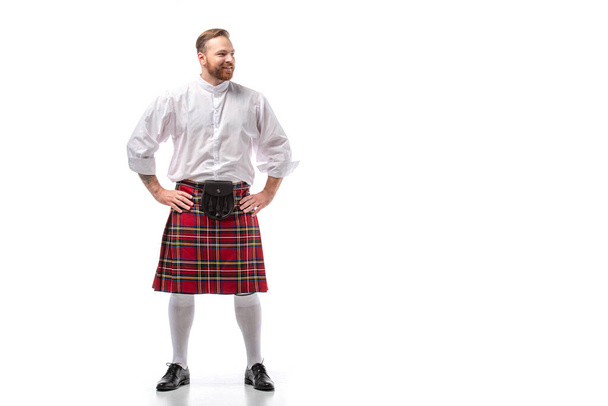 Посмішка шотландського рудого чоловіка в червоному кілті з руками на бедрах на білому тлі - Фото, зображення