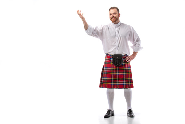 smiling Scottish redhead man in red kilt pointing with hand on white background - Photo, Image