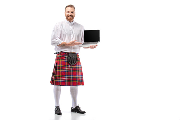 mosolygós skót vörös hajú férfi piros skót szoknya gazdaság laptop üres képernyő fehér háttér - Fotó, kép