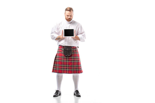 sad Scottish redhead man in red kilt presenting digital tablet on white background - Fotó, kép