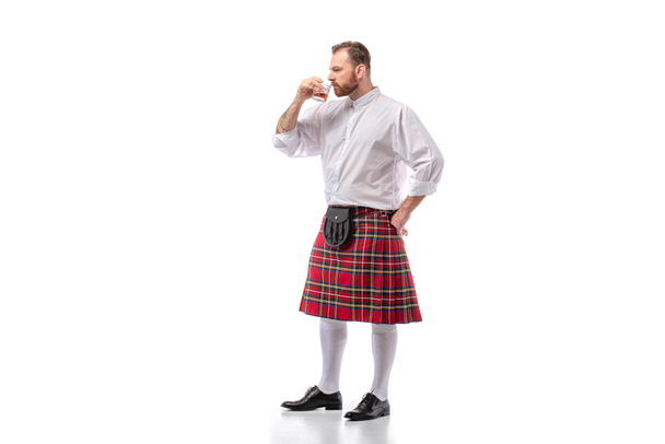 Schotse roodharige man in rode kilt ruikt whisky op wit - Foto, afbeelding