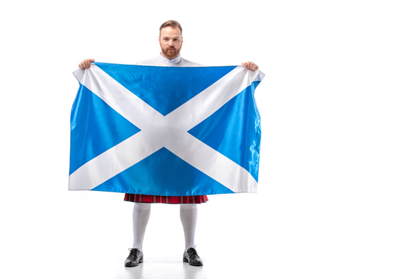 Scottish redhead man in red kilt with flag of Scotland on white background - Zdjęcie, obraz