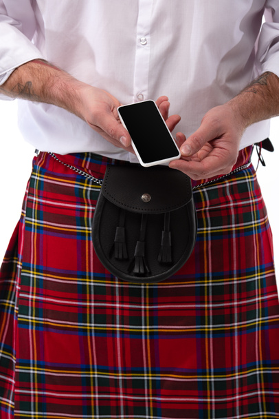 oříznutý pohled na skotského muže v červeném kiltu s koženým opaskem a smartphonem izolovaným na bílém - Fotografie, Obrázek