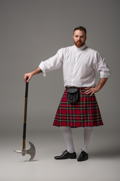 Hombre pelirrojo escocés en escocés rojo con hacha de batalla sobre fondo gris
 - Foto, Imagen