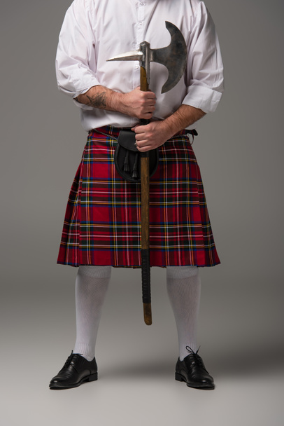 καλλιεργημένη άποψη του Σκωτσέζου άνδρα σε κόκκινο κιλτ με τσεκούρι μάχης σε γκρι φόντο - Φωτογραφία, εικόνα