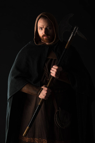 frowning medieval Scottish warrior with battle axe in mantel isolated on black - Foto, imagen