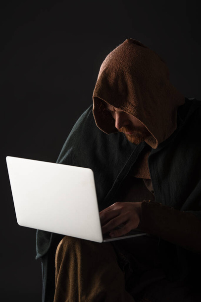 médiéval écossais homme dans mantel en utilisant ordinateur portable dans l'obscurité isolé sur noir
 - Photo, image