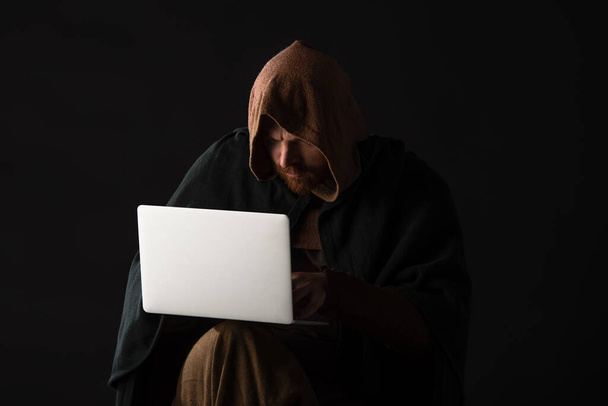 medieval Scottish man in mantel using laptop in dark isolated on black - Foto, immagini