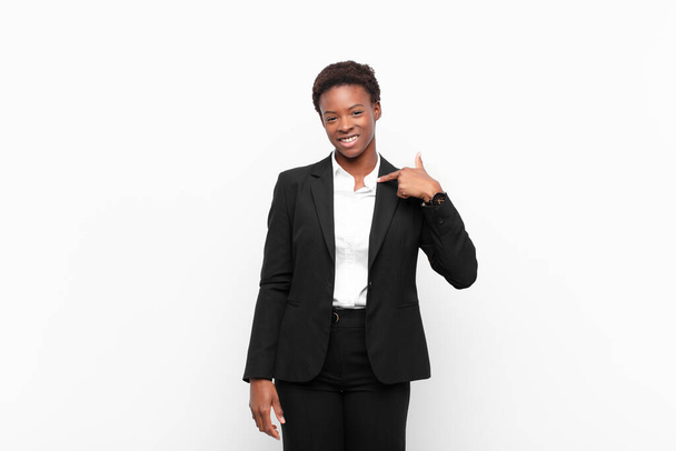 young pretty black womanlooking happy, proud and surprised, cheerfully pointing to self, feeling confident and lofty against white wall - Фото, зображення