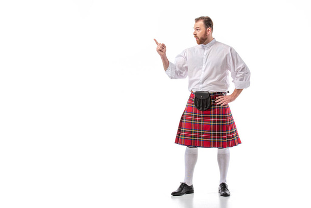 Scottish redhead bearded man in red tartan kilt pointing with finger on white background - Photo, Image