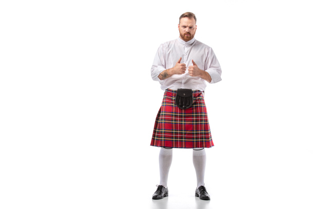 Scottish redhead bearded man in red tartan kilt showing thumbs up on white background - Foto, Bild