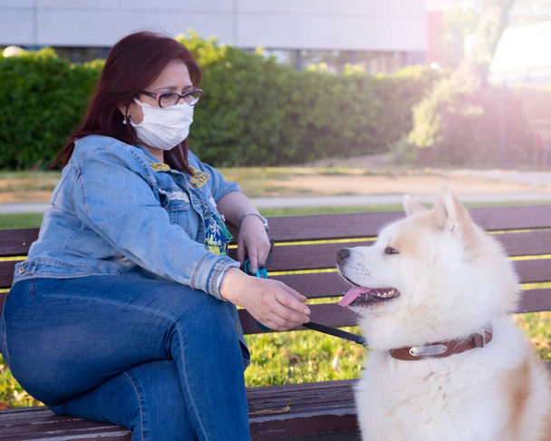woman sits in a park van with her dog, and medical mask, by quarantine, covid-19 - Foto, Bild