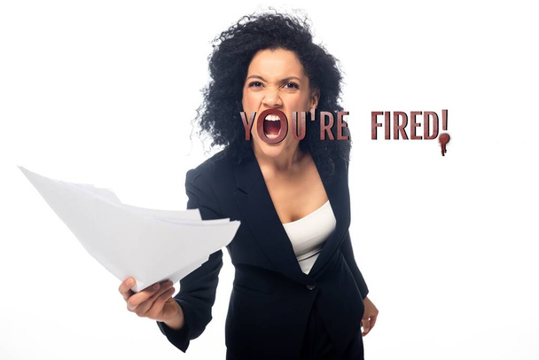 Enojada mujer de negocios afroamericana con papeles gritando que estás despedida aislada de blanco
 - Foto, Imagen