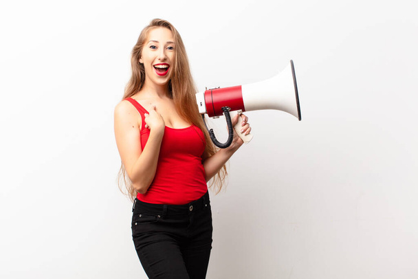 yound blonde woman feeling happy, surprised and proud, pointing to self with an excited, amazed look holding a megaphone - Φωτογραφία, εικόνα