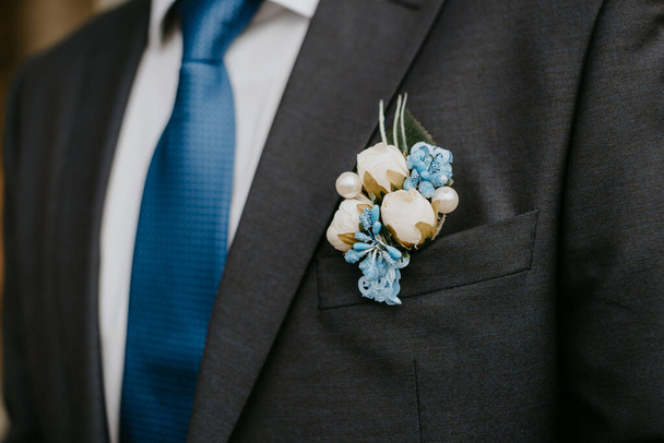Τεχνητό λουλούδι μπουτονιέρα στο μπλε σακάκι του γαμπρού - Φωτογραφία, εικόνα