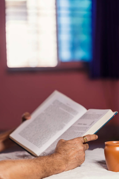 Hombre indio leyendo libro y en auto-aislamiento en casa durante el bloqueo del virus corona. Antecedentes para la autocuarentena covid-19, relajación, jubilación, pasatiempo, distanciamiento social
. - Foto, Imagen