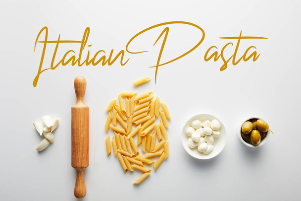 Flat lay with garlic, rolling pin, pasta and bowls with olives and mozzarella on white background, italian pasta illustration - Photo, image