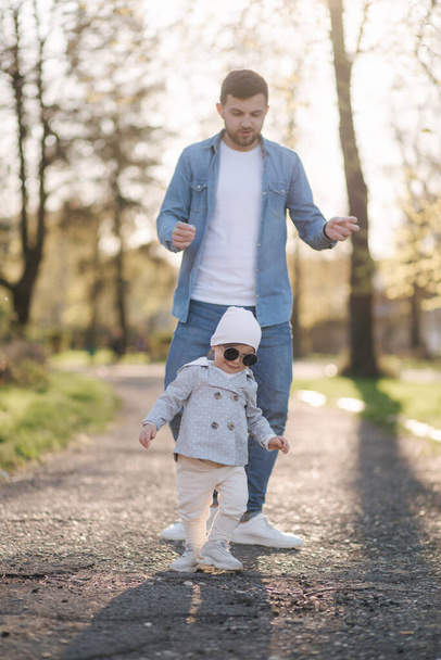 La adorable pequeña Gilr pasa tiempo con su padre. Papá y su hija caminan por el parque. Una familia con estilo. Niña feliz con gafas de sol. Papá y su hija bailan en el parque
 - Foto, imagen