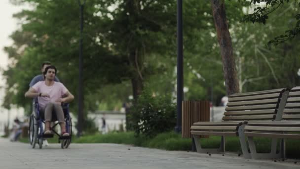 Feliz hombre discapacitado en una silla de ruedas con joven feliz corriendo en el parque de la ciudad
 - Imágenes, Vídeo