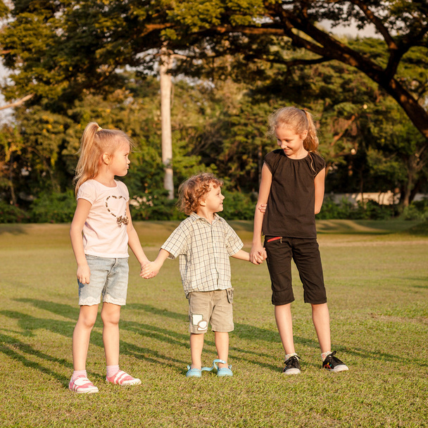 трое счастливых маленьких детей играют в парке в дневное время
 - Фото, изображение