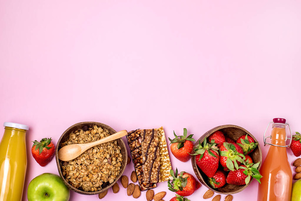 Breakfast Concept Healthy Diet Food Coconut Bowl with Muesli Bowl with Ripe Strawberry Green Apple Muesli Bars Bottles of Citrus Juice Pink Background Horizontal Copy Space - Photo, Image